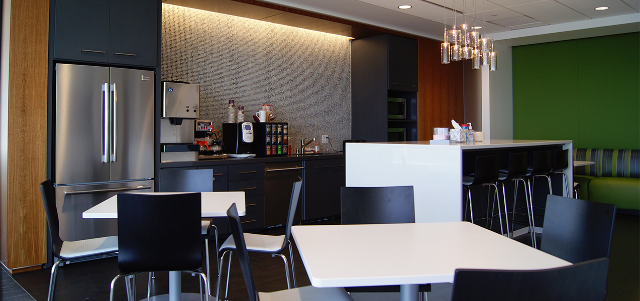 Break room area featuring coffee maker, counter, fridge and tables inside the Tri-North Builders CBRE construction project.