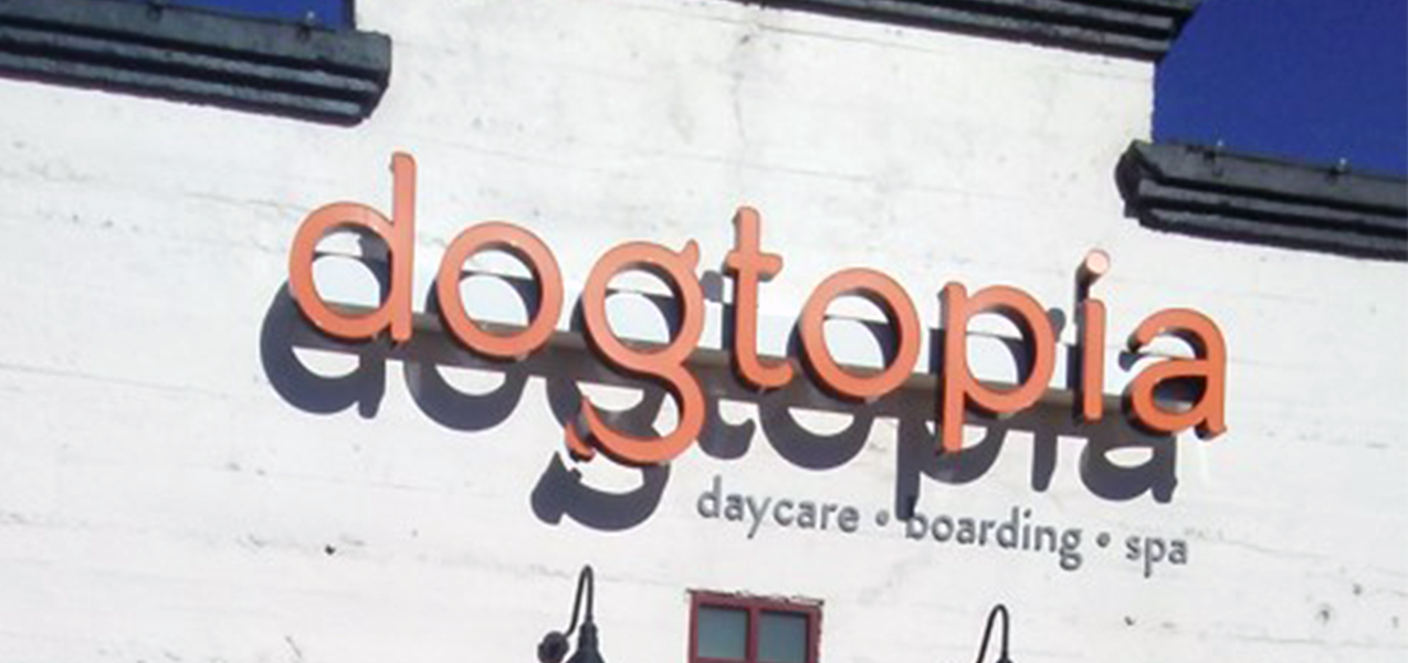 The Dogtopia sign is seen against the white brick facade of one groomer location.