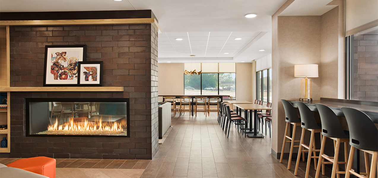 Tables, chairs & fireplace inside Tri-North Builders project at Home2Suites by Hilton Madison Central Alliant Energy Center.