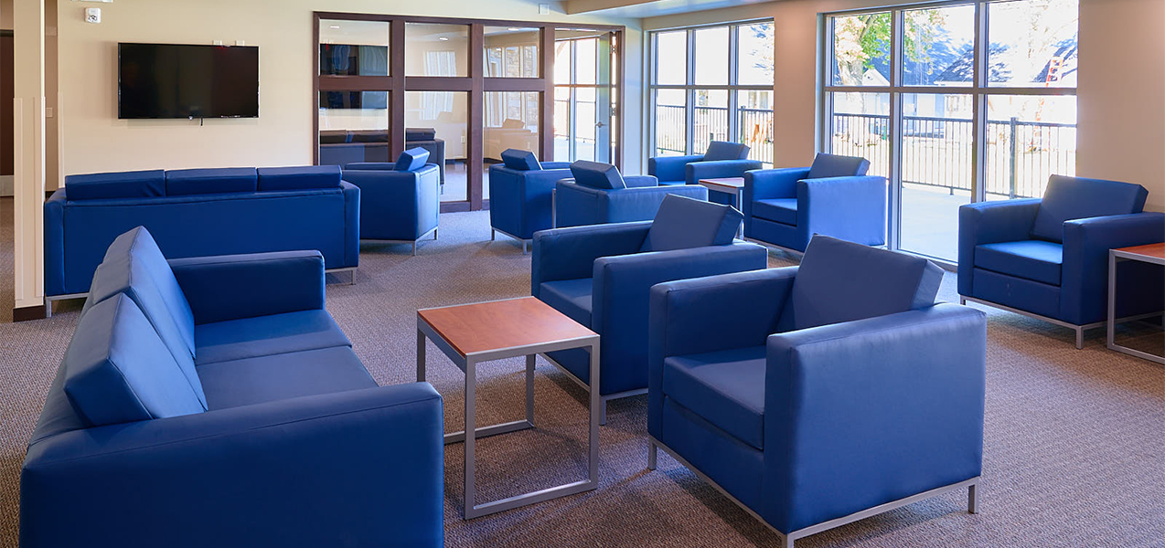 Common room with blue chairs, tables and window inside the Newman Heights apartment building built by Tri-North Builders.