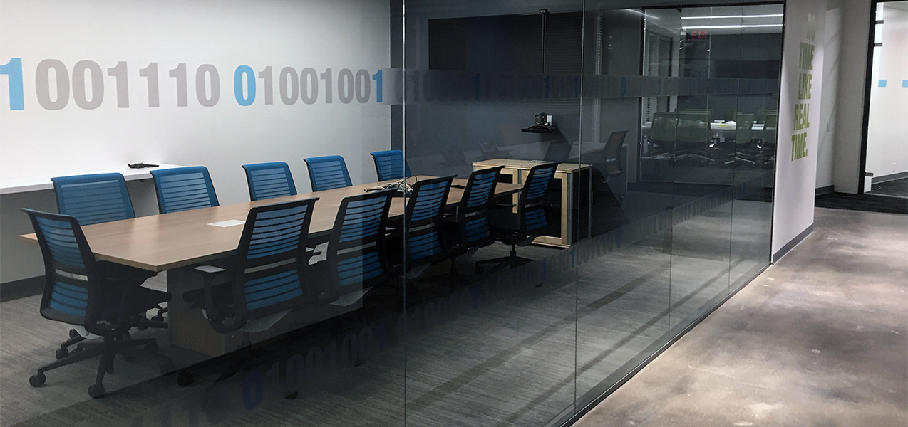 A glass wall offers a view of a conference table and chairs at the NICE office built by Tri-North.