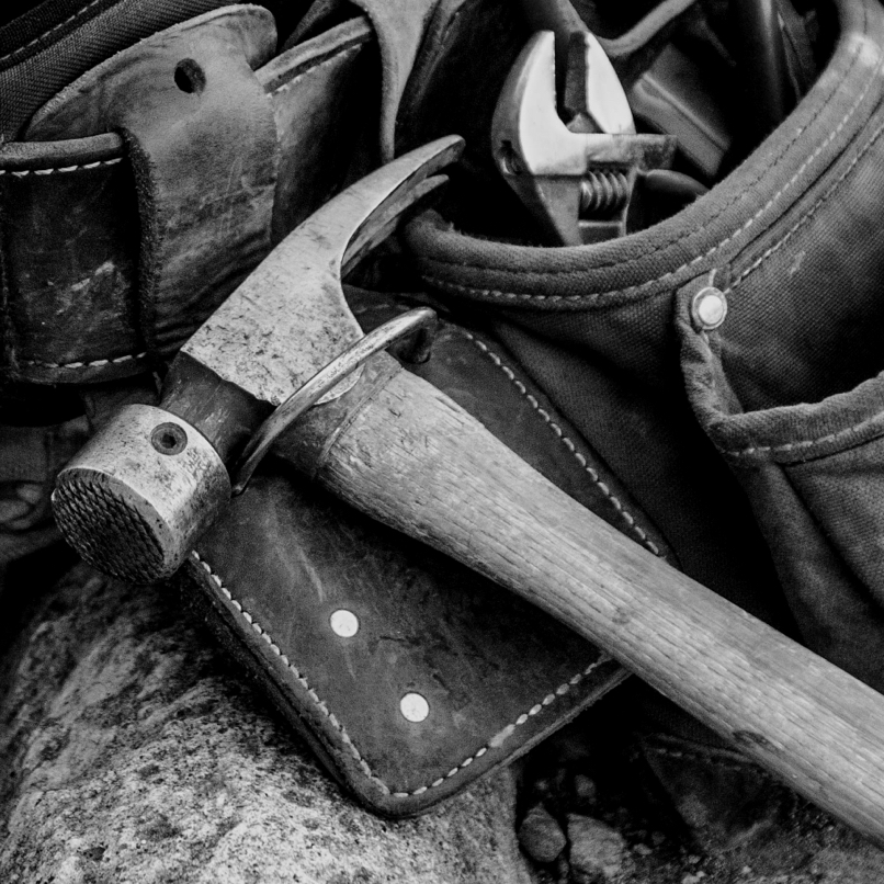 A hammer rests on a leather tool belt.